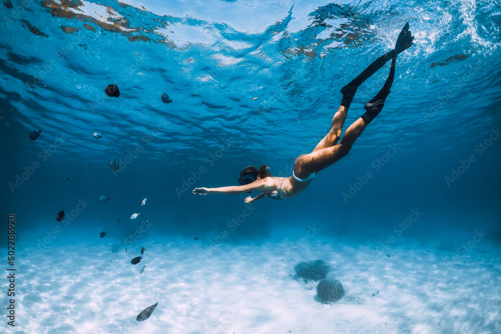 Attractive woman freediver with fins glides over sandy bottom. Freediving in blue ocean