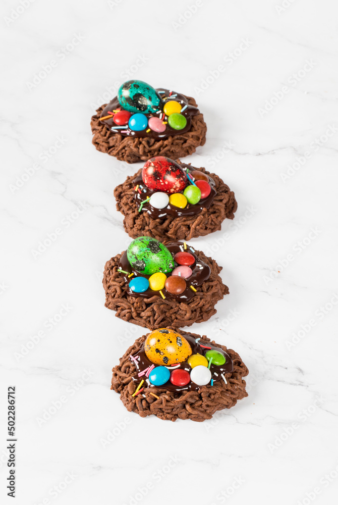Holiday dessert. Easter chocolate cookie in the shape of a nest, decorated with a quail egg and colorful candy dragees and confectionery sprinkles. White background