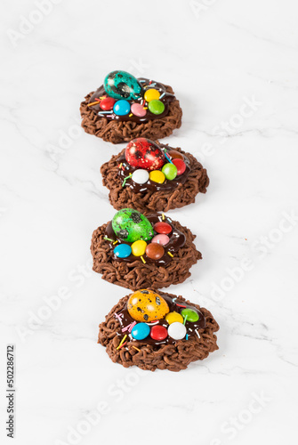 Holiday dessert. Easter chocolate cookie in the shape of a nest, decorated with a quail egg and colorful candy dragees and confectionery sprinkles. White background