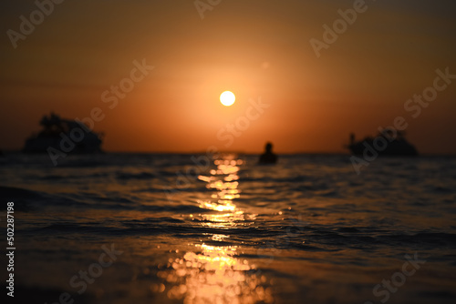 Caribbean beach sunset, with the sun setting on the horizon, with a boat sailing along the beach