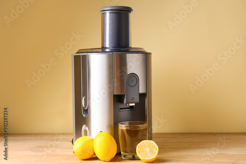 New modern juicer and glass of fresh juice with lemons on wooden table