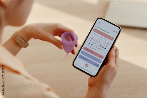 Close up of young woman calculating menstrual cycle using mobile app calendar, copy space photo