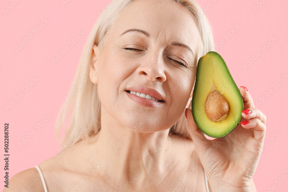Mature blonde woman with avocado on pink background, closeup Mature blonde woman with avocado on pink background, closeup