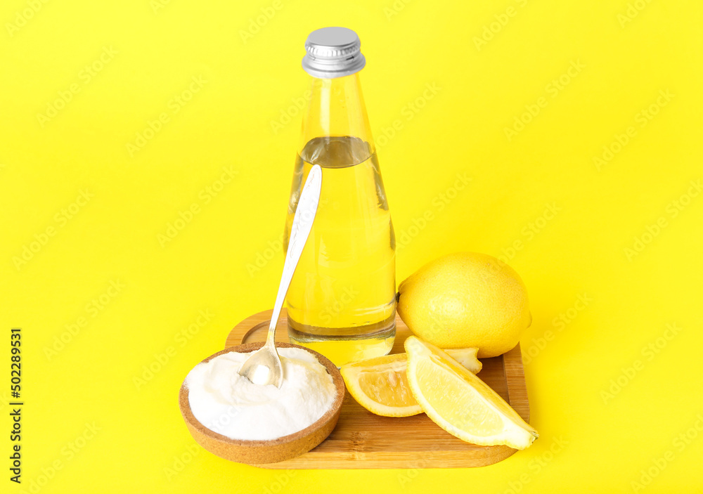 Wooden board with bottle of water, lemon and baking soda on yellow background Wooden board with bottle of water, lemon and baking soda on yellow background