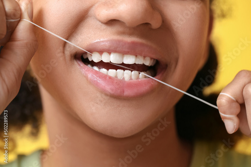 African-American teenage girl flossing teeth on yellow background, closeup