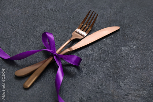 Knife and fork with ribbon on dark background