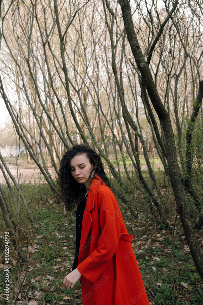 portrait of curly brunette woman in red coat in the park portrait of curly brunette woman in red coat in the park