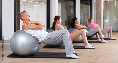 Sporting people practicing Pilates in the studio during a group training session perform a back stretching exercise with ..a ball