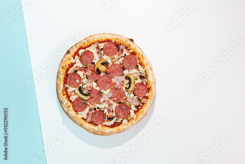 Italian pizza with salami, bacon and mushroom on coloured background. Meat pizza with salami and bacon in minimal style on blue and orange color. American pizza delivery concept with color backdrop