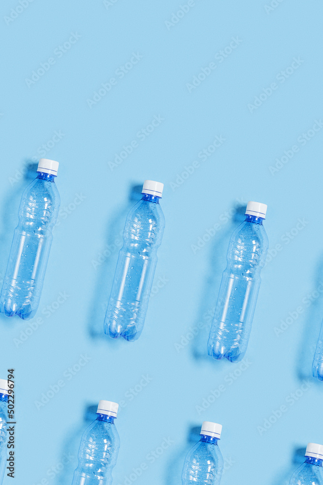 Pattern with blue plastic bottles on blue paper background, top view empty plastic bottle for water half litre, minimal image. Pollution, plastic garbage, environmental protection concept Pattern with blue plastic bottles on blue paper background, top view empty plastic bottle for water half litre, minimal image. Pollution, plastic garbage, environmental protection concept