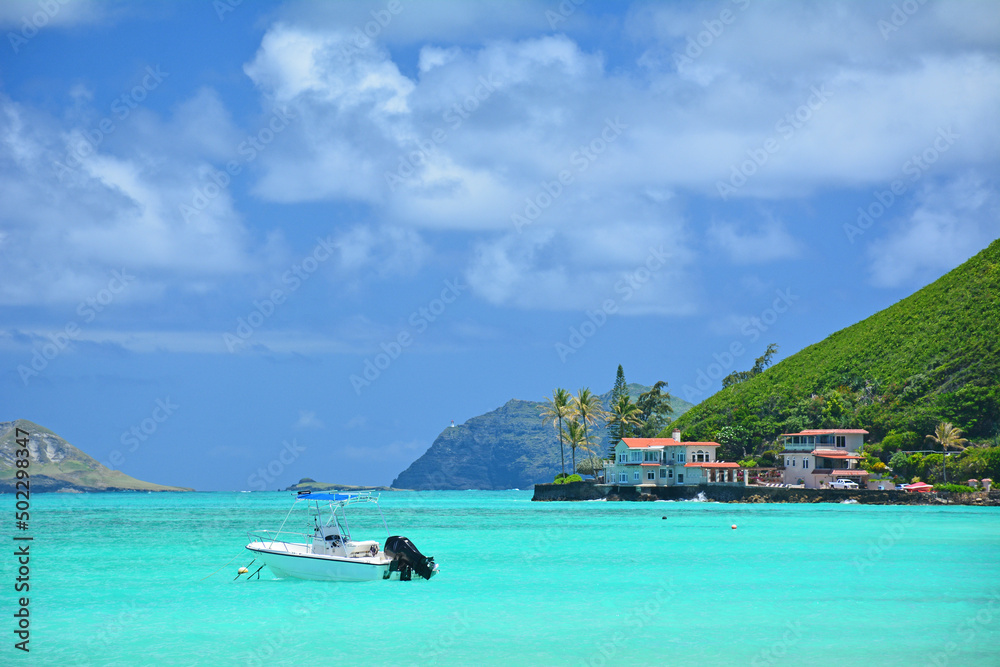 Obraz premium Boat anchored in calm, turquoise waters on a clear sunny day at Lanikai Beach on the windward side of Oahu, Hawaii. 