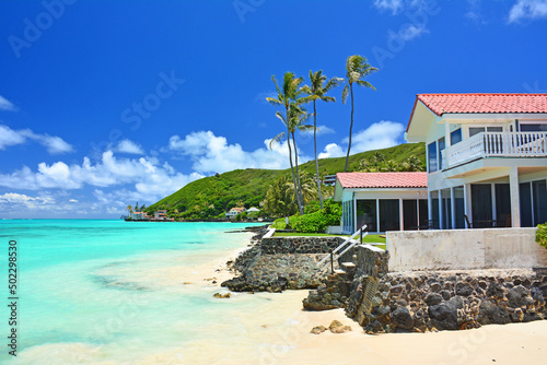 Fototapeta Naklejka Na Ścianę i Meble -  Oceanfront beach home with turquoise waters and swaying palm trees on a clear sunny day at Lanikai Beach on the windward side of Oahu, Hawaii. 