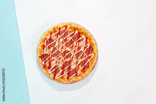Italian pizza with ham and salami on coloured background. Meat pizza with ham, ketchup and mayonnaise in minimal style on blue colour. American pizza delivery concept with color backdrop