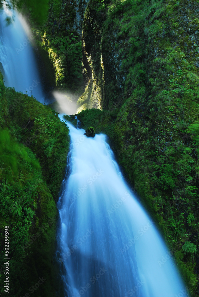 Naklejka premium Blue two stage waterfall flowing down a green mountain