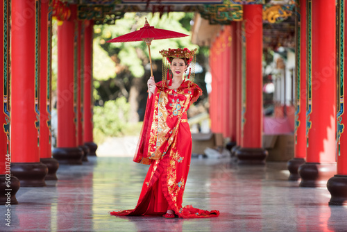 woman in traditional costume. Beautiful young woman in a bright red dress and a crown of Chinese Queen posing against the ancient door. Chinese Letter meaning about the happiness pavilion.