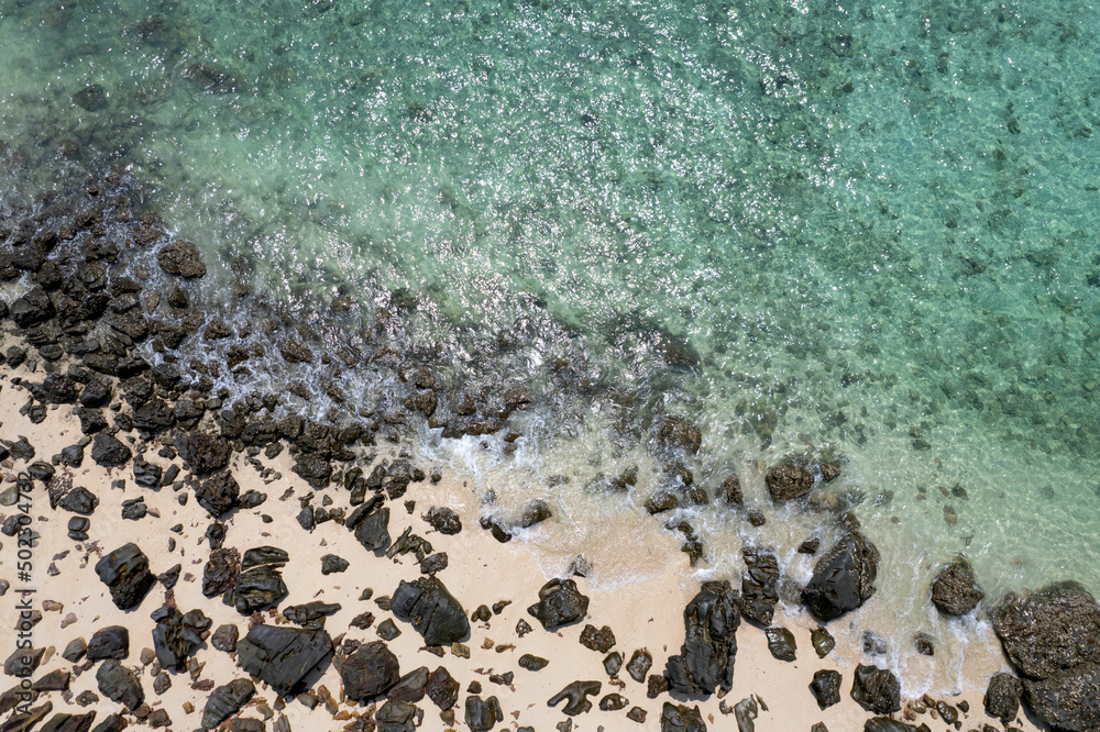 Aerial view of sea water blowing towards the beach. The beach has black rocks, contrasting with the sea sand. Amazing beauty.on the island of the Andaman Sea