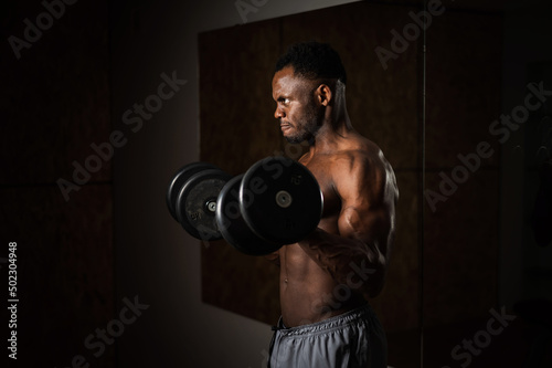 Muscular dark-skinned man doing an exercise with dumbbells. 