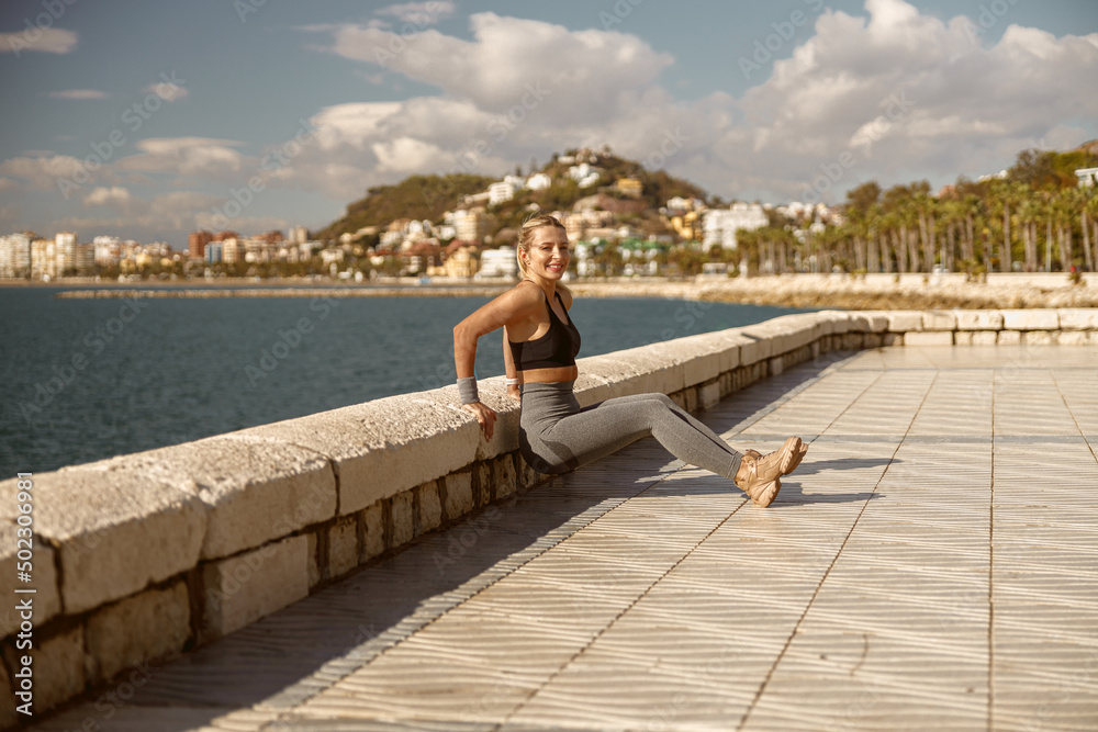 Smiling young sportswoman doing warm-up exercise near sea