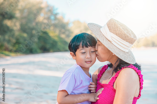 Asian boy and mom woman relaxing on tropical beach, they are njoy freedom and fresh air, wearing stylish hat and clothes. Happy smiling tourist in tropics in travel vacation