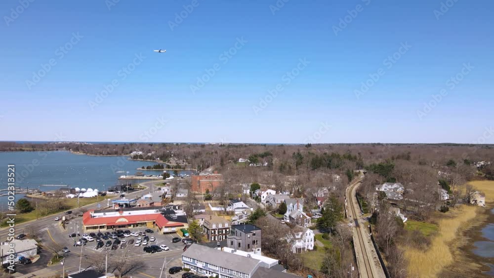 Plane flies across a blue, clear sky without clouds over a small town next to a lake with train station. Drone static shot. Plane flies across a blue, clear sky without clouds over a small town next to a lake with train station. Drone static shot.