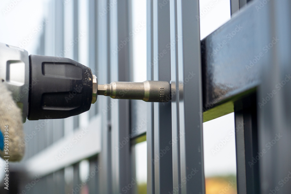 Close-up of screwing roofing screws into a metal picket fence. Installing the fence Close-up of screwing roofing screws into a metal picket fence. Installing the fence