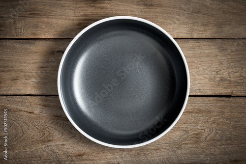 Top view of blank black food plate on a wood background with copy space.