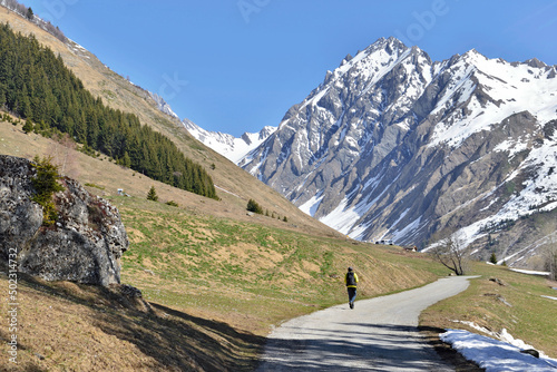 rocky mountain still snowed in spring at the end of a road where walks the silhouette of a hiker in the franch Alps photo