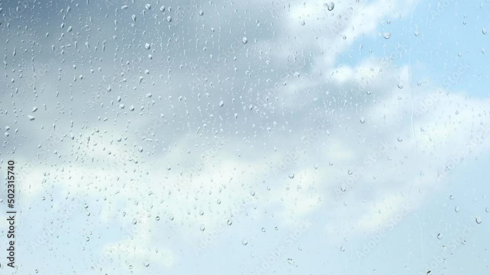 Rain drops on window surface against cloudy sky. Streams of water flow down the glass, close up. Rain drops on window surface against cloudy sky. Streams of water flow down the glass, close up.