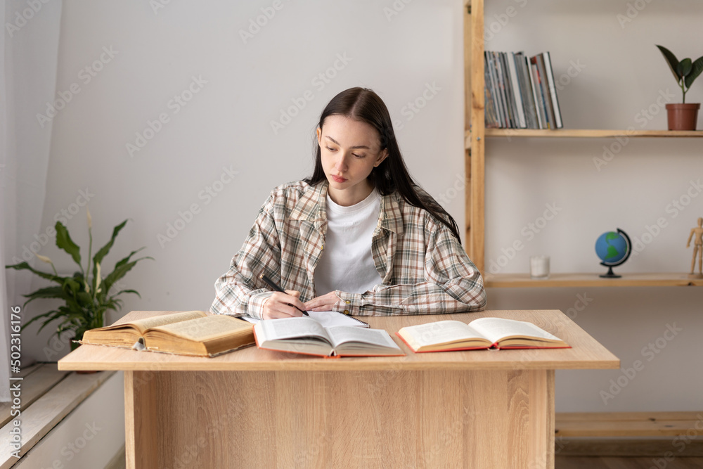 Distance education, girl student studying at home doing homework using a lot of books, studying a school subject, preparing a biology project, home schooling Distance education, girl student studying at home doing homework using a lot of books, studying a school subject, preparing a biology project, home schooling