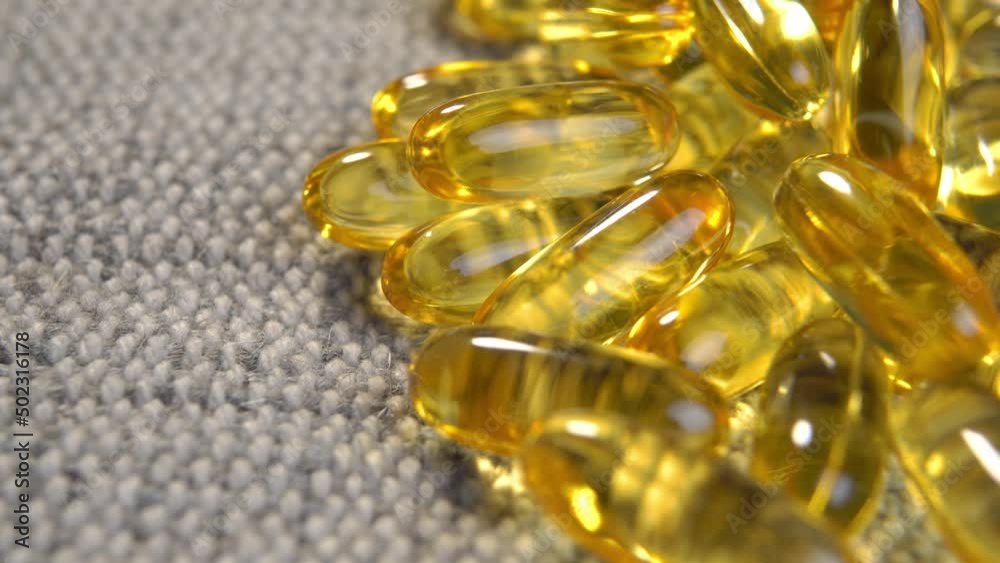 Yellow translucent Omega 3 capsules with fish oil supplement on rustic jute cloth. Alternative medicine concept. Macro. Rotation Yellow translucent Omega 3 capsules with fish oil supplement on rustic jute cloth. Alternative medicine concept. Macro. Rotation