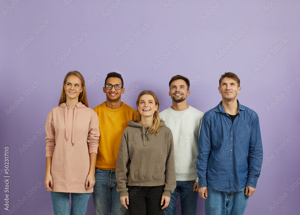Happy diverse multiethnic young people isolated on violet studio background look up at sale deal or promotion. Smiling millennial group or team think of discount or offer. Copy space, advertising. Happy diverse multiethnic young people isolated on violet studio background look up at sale deal or promotion. Smiling millennial group or team think of discount or offer. Copy space, advertising.