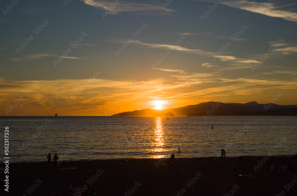 Amazing sunset on the ocean - blue cloudy sky background, sun path on the ocean and people silhouette