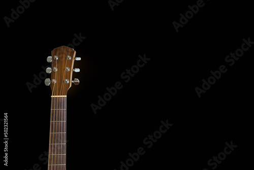Isolated head of acoustic guitar leaned against the dark blackbackground. Copy space.