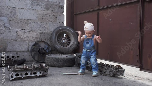 serious little girl in overalls with wrench in her hands among spare parts