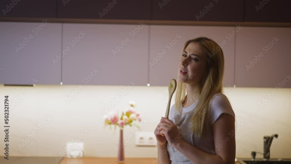 Expressive lady sings using spoon with salad leaf as microphone and dances during dinner making in modern kitchen at home slow motion Expressive lady sings using spoon with salad leaf as microphone and dances during dinner making in modern kitchen at home slow motion