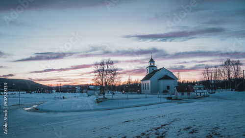 Sweden Jämtland (Lapland). The church of Storsjö, a cozy town next to Ljungdalen during blue hour. Snow is melting under dramatic violet sky. photo