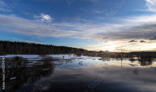 Epic spring landscape by the river. The flood of the river in early spring. A colorful sunset is reflected in the water. March evening landscape. © Sergei
