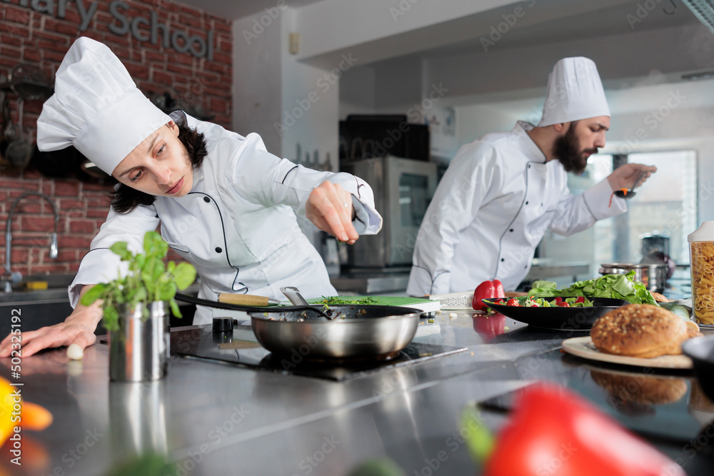 Fine dining restaurant head chef seasoning gourmet dish and adding chopped fresh herbs and greens. Cuisine cook preparing meal for dinner service while in professional kitchen.