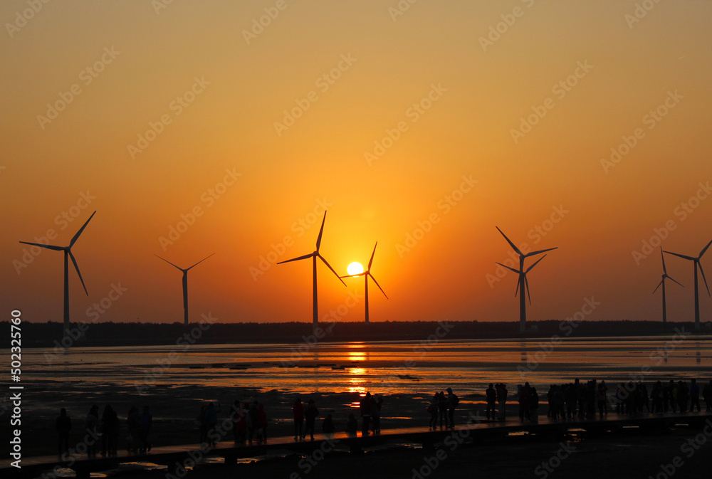 The red sky and sunset reflect the sea and the silhouette windmill with the sandy beach in the distance, natural scenery background.