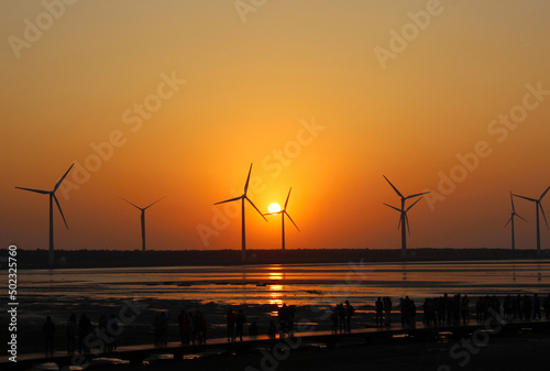 The red sky and sunset reflect the sea and the silhouette windmill with the sandy beach in the distance, natural scenery background.