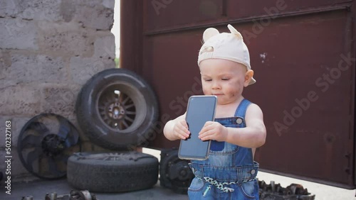 Kid mechanic holds phone in his hands and shakes it. In background auto parts