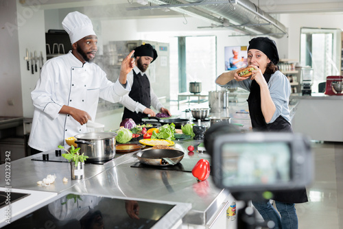 Gastronomy experts in restaurant professional kitchen cooking gourmet dish while recording culinary course. Chefs shooting video about meal preparing process while broadcasting on television program.