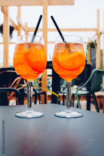 Two glasses of Aperol Spritz served on the terrace of modern bar. Popular Italian wine based cocktail and summer aperitif refreshing drink prepared with prosecco wine, bitter liqueur and soda water.