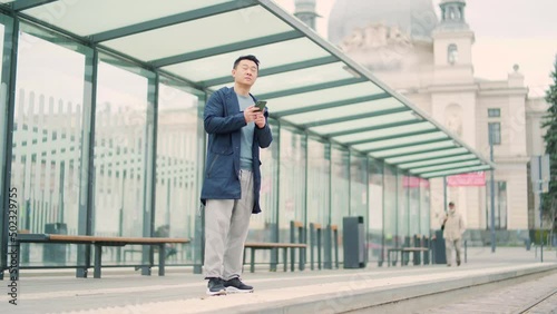 Wallpaper Mural Asian man using phone at bus or tram stop. Asian people use smartphone waiting for bus station, orders a taxi application on the phone, book accommodation online for business travel Torontodigital.ca