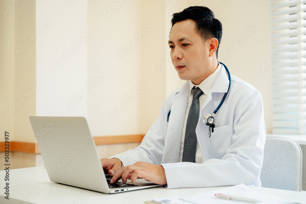 Male Doctor expert wearing white coat using laptop and reading clipboard report at work in hospital. Male Doctor expert wearing white coat using laptop and reading clipboard report at work in hospital.
