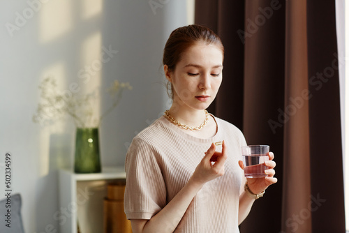 Fototapeta Minimal portrait of young woman holding vitamin capsule and taking supplements w