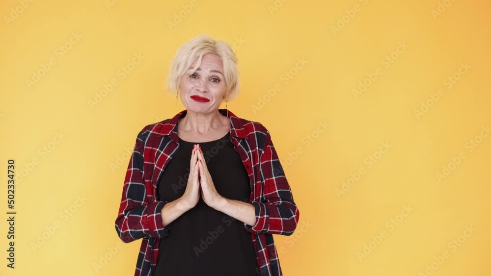 Sincere request. Begging woman. Desperate feelings. Pleading funny middle-aged lady holding hands in praying gesture asking favor isolated yellow.