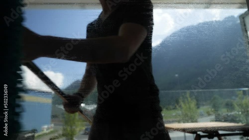 Young hipster houseman cleaning dirty window with towel and glas scraper