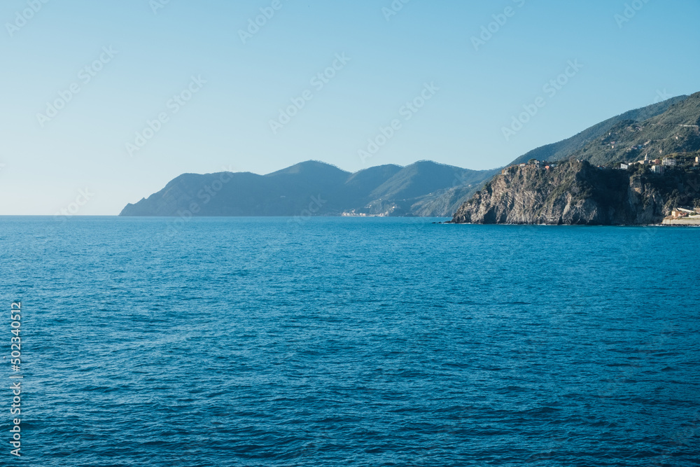 Beautiful seascape with blue sky, smooth water surface and rocky cliffs in Liguria coastal area. Popular italian travel destination.