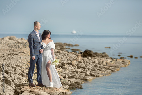 a young man in a suit and a girl in a wedding dress are standing on the seashore.